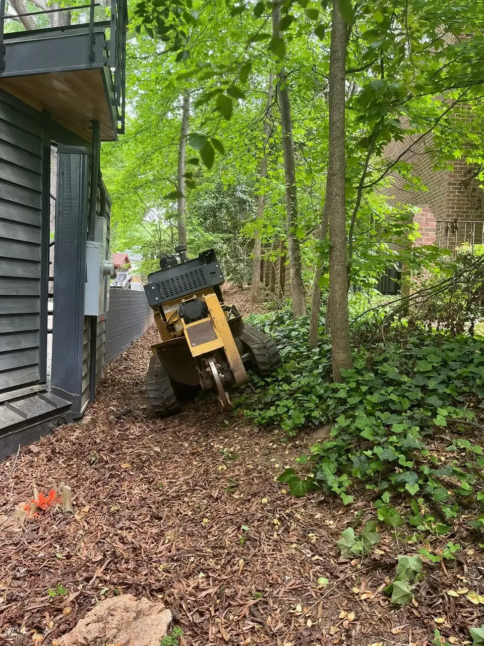 Home 13 Fonvilletreeservice tracked stump grinder machine positioned near tree stumps in wooded residential backyard area in NC